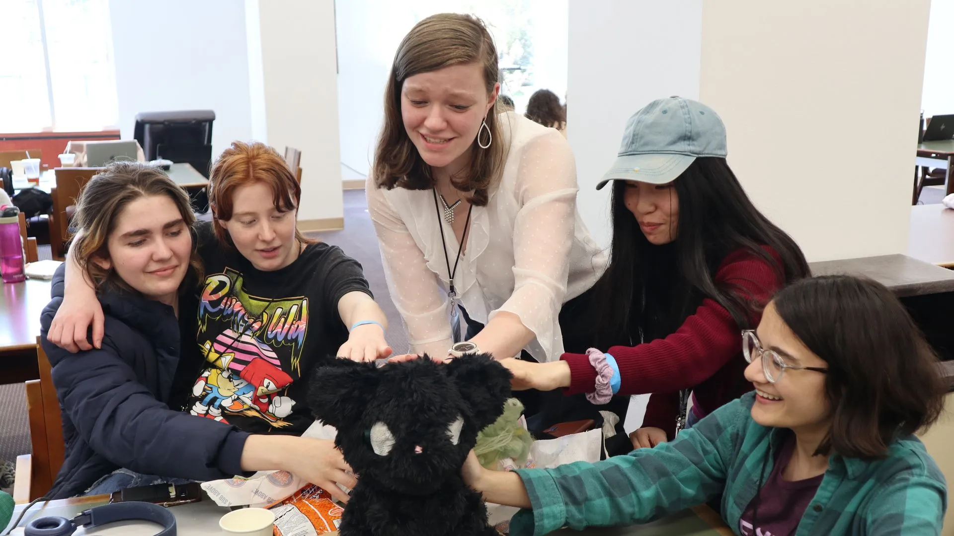 Five people smiling and petting a stuffed robot cat